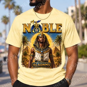 Op de afbeelding: Een lichtgeel t-shirt met een grafische print van een Egyptische farao met een blauwe en gouden hoofdtooi en kraag. Het ontwerp bevat palmbomen, piramides, een zon, het woord NOBLE in gouden letters en de tekst AEAONMS onderaan.