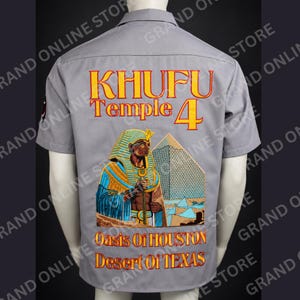 May include: A light grey short-sleeve button-down shirt featuring a large back graphic of an Egyptian pharaoh and a pyramid. The text reads KHUFU Temple 4, Oasis Of HOUSTON, and Desert Of TEXAS in yellow and red lettering on the back of the shirt.