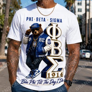 May include: A white short-sleeve t-shirt featuring a graphic of a brown bear wearing a blue and white varsity jacket, a blue cap with the letters ΦΒΣ, and blue sneakers. The text reads PHI BETA SIGMA, 1914, and Blu Phi Till The Day I Die.
