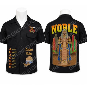 May include: A black short-sleeve button-down shirt featuring a front graphic of a camel and pyramids with the text AEAONMS and Desert Rider. The back displays a large graphic of an Egyptian figure, pyramids, and the word NOBLE in yellow and green.