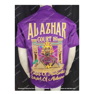 May include: Purple short-sleeved shirt with a gold embroidered design featuring a woman in a crown, pyramids, and the text "Al Azhar Court 181 Oasis of Huntsville Desert of Alabama".