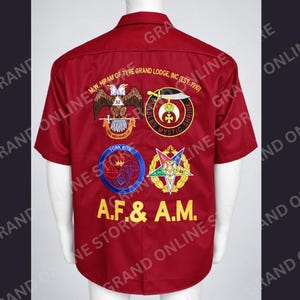 May include: A short-sleeved, button-down shirt in deep red featuring embroidered emblems on the back. The text reads M.W. HIRAM OF TYRE GRAND LODGE, INC (EST. 1910), NOBLES MYSTIC SHRINE, YORK RITE, and A.F. & A.M. with various fraternal symbols.