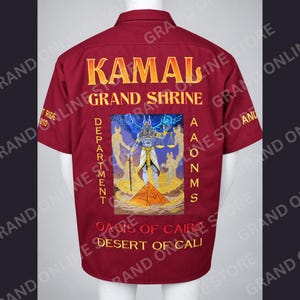 May include: A maroon short-sleeved button-down shirt featuring embroidered yellow text that reads KAMAL GRAND SHRINE, DEPARTMENT, AAONMS, OASIS OF CAIRO, and DESERT OF CALI. A central graphic depicts an Egyptian deity holding scales above a pyramid.