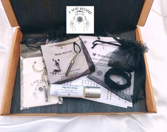 May include: A cardboard box containing a Soul Whisper protection kit with a roller bottle, a black salt vial necklace, a black cord, and printed cards. The items are packaged in black organza bags and clear plastic sleeves with branding.