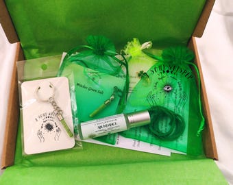 May include: A cardboard box containing a keychain with a green vial, a small bag labeled Witches Green Salt, a green organza bag with a clover charm, and a roller bottle labeled Soul Whisper Abundance with a green cord.