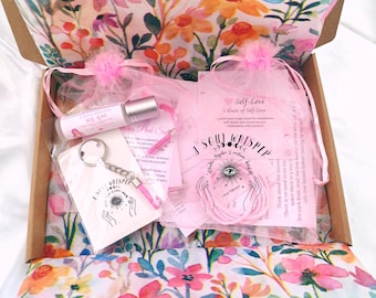 May include: A cardboard gift box lined with floral paper containing a roller bottle labeled Soul Love, a keychain with a Soul Whisper card, a pink string, and a Self-Love card. The items feature pink accents and printed text including Soul Whisper.