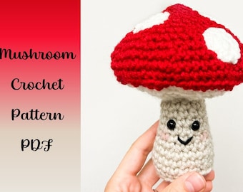May include: A crocheted mushroom amigurumi toy with a red and white cap and a beige stem with a smiling face. The mushroom is being held in a hand.