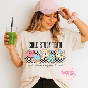 May include: Cream-colored t-shirt with the text "CHILD STUDY TEAM" in black. The shirt features colorful cartoon graphics of a heart, a planet, a laptop, and a globe. The words "referral-evaluation-eligibility-IEP-repeat" are printed below the graphics.