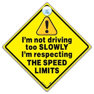 May include: Yellow diamond-shaped car sign with a black exclamation point inside a black triangle. The sign reads "I'm not driving too SLOWLY I'm respecting THE SPEED LIMITS".