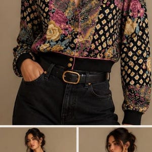 May include: Black bomber jacket with a floral and geometric pattern in pink, yellow, and purple. The jacket has a black collar, cuffs, and waistband, and is paired with black jeans and a gold belt. The jacket is buttoned up.