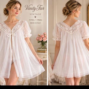 Könnte beinhalten: Ein weißer, transparenter Bettmantel mit kurzen Puffärmeln, einem V-Ausschnitt mit floraler Spitzenborte und einer Bindeschleife vorne. Das Kleidungsstück hat eine ausgestellte Silhouette und den Text Vanity Fair VINTAGE 1950s / 1960s BED COAT.