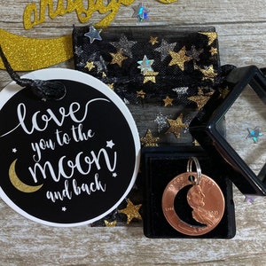 May include: A collection of celestial-themed items, including a gold glittery moon and stars cutout with the phrase "Love you to the moon and back." Also, a black and white tag with the same phrase, a penny pendant, and a black mesh bag.