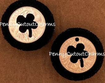 May include: Two coin charms with a cutout clover design, set in black felt circles. The coins are copper-coloured, and one has a small hole at the top. The text "PennyCutoutCharms" is visible.