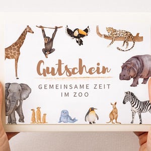 Pode incluir: Um vale-presente creme com ilustrações em aquarela de animais do zoológico, incluindo uma girafa, um macaco, um tucano, um leopardo, um hipopótamo, um elefante, suricatas, uma foca, um pinguim, um canguru e uma zebra. O texto "Gutschein" e "Gemeinsame Zeit im Zoo" é impresso em marrom.