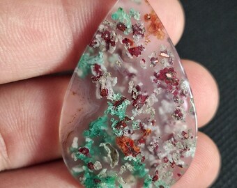 May include: A teardrop-shaped pendant made of clear agate with inclusions of green, red, and white. The pendant is translucent and has a natural, organic look.