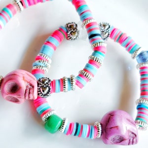 May include: Two colorful bracelets with pink and blue beads, silver spacers, and pink skull charms.