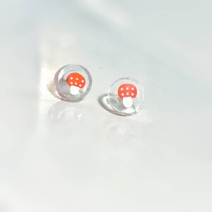May include: A pair of clear stud earrings with a red and white mushroom design.