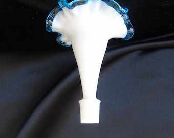 Pode incluir: Uma rolha de garrafa de vidro branco com uma parte superior alargada e uma borda azul com babados. A rolha tem um pescoço longo e fino e uma base quadrada. O design é elegante e decorativo.