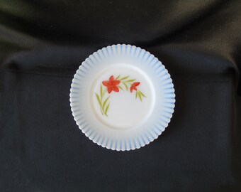 May include: A white milk glass plate with a blue scalloped edge and a red flower design.