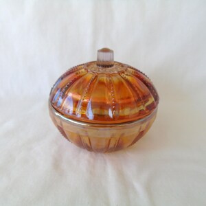 May include: A vintage amber glass candy dish with a domed lid. The dish has a ribbed design and a silver trim around the edge.
