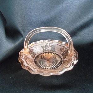 May include: A pink glass candy dish with a handle. The dish is decorated with a floral pattern and has a scalloped edge.