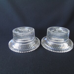 May include: Two clear glass candle holders with a fluted design. The holders have three small indentations on the top for candles.