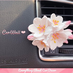 May include: White and pink flower car air freshener with the text "Car Waii" in pink lettering.