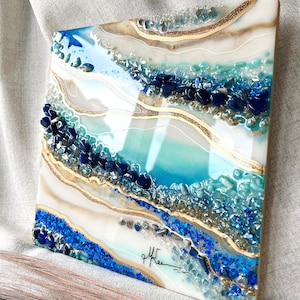 Könnte beinhalten: Abstrakte Harz-Kunstmalerei in den Farben Blau, Weiß und Gold. Das Gemälde zeigt ein geschichtetes Design mit eingebettetem blauem und goldenem Glitzer und kleinen blauen und grünen Steinen. Das Gemälde ist unten rechts mit "gffren" signiert.