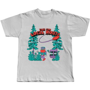 May include: White t-shirt with a graphic of a person throwing a disc in a forest. The graphic includes the text "Take the Local Route".