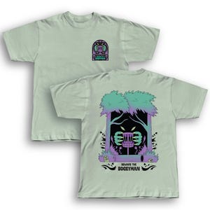Puede incluir: Dos camisetas verde claro. Una camiseta tiene un peque&ntilde;o gr&aacute;fico en la parte delantera. La otra camiseta tiene un gr&aacute;fico m&aacute;s grande en la parte posterior con una canasta de disc golf, &aacute;rboles y el texto "Beware the Boogeyman."