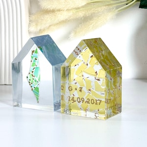 May include: Two small glass house-shaped ornaments. One is clear with a green and gold mosaic inside. The other is yellow with gold flecks and the text "C G + T 14.09.2017".