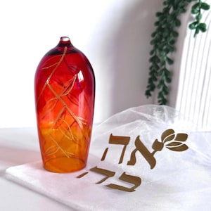 Peut inclure: Un récipient en verre haut et arrondi présentant un dégradé vibrant allant du rouge profond au sommet à l'orange vif à la base. La surface est ornée d'un délicat motif de branche gravé de couleur dorée. À côté se trouve une pochette en tissu blanc.