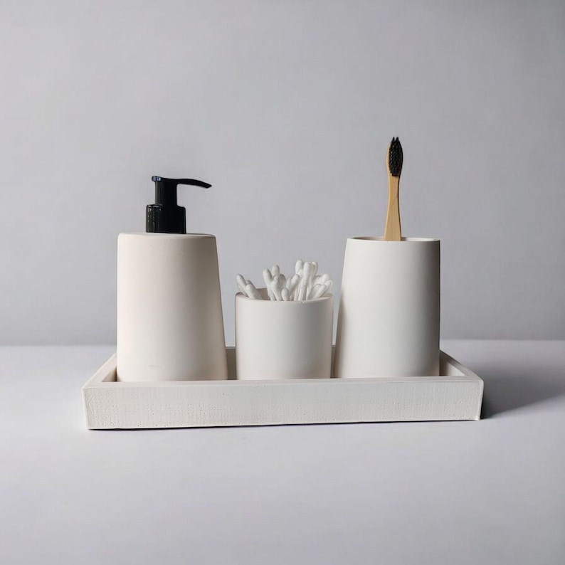 May include: White ceramic bathroom countertop organizer with three compartments. The organizer includes a pump bottle, a cotton swab holder, and a toothbrush holder. The organizer is on a white tray.