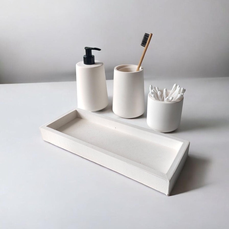 May include: White ceramic bathroom countertop organizer set with a tray, soap dispenser, toothbrush holder, and cotton swab container.