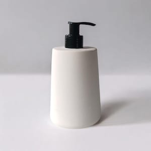May include: White ceramic soap dispenser with a black pump. The dispenser has a rounded, cylindrical shape.