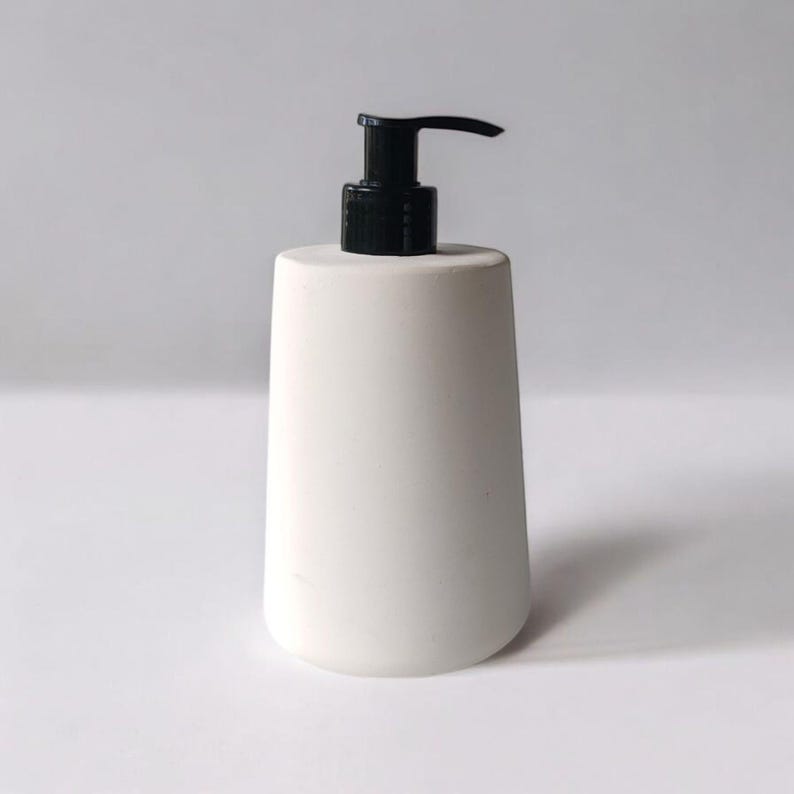 May include: White ceramic soap dispenser with a black pump. The dispenser has a rounded, cylindrical shape.