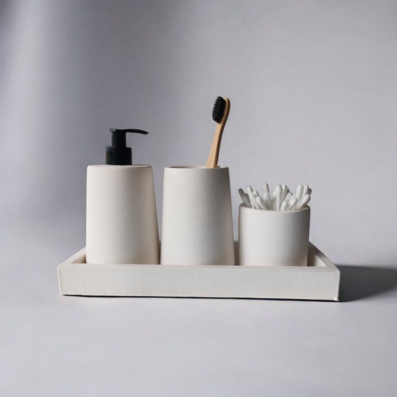 May include: White ceramic bathroom countertop organizer with a tray, two cups, and a pump bottle. The organizer includes a toothbrush and cotton swabs.