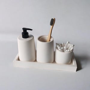 May include: White ceramic bathroom countertop organizer with three compartments. The organizer includes a soap dispenser, a toothbrush holder, and a cotton swab holder.