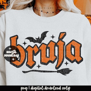 Può includere: Una felpa bianca a girocollo con il testo arancione bruja in un carattere grassetto e usurato. Il design include una sagoma di pipistrello nero sopra le lettere, piccole stelle a quattro punte e una scopa nera sotto il testo.