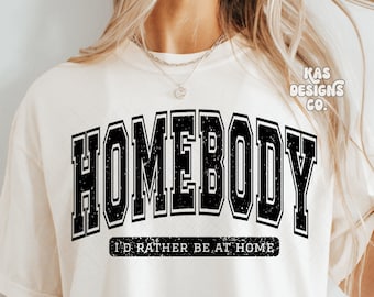 May include: A white t-shirt with black text that reads "HOMEBODY I'D RATHER BE AT HOME". The text is in a distressed font style.