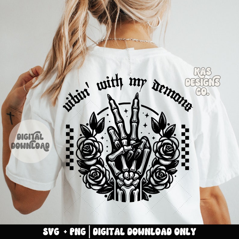 May include: A white t-shirt featuring a black graphic design of a skeleton hand making a peace sign with roses and the text "vibin' with my demons".