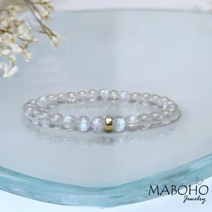 May include: A white moonstone beaded bracelet with a gold accent bead. The bracelet is on a white surface.