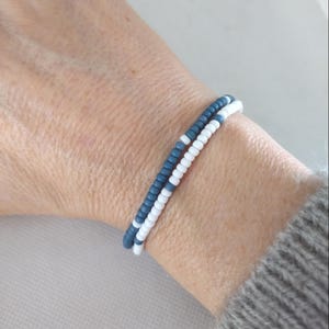 May include: A bracelet made of white and blue beads. The bracelet is on a person's wrist.
