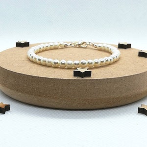 May include: A white pearl bracelet with a silver clasp. The bracelet is on a wooden surface with small wooden stars.