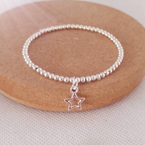 May include: A silver beaded bracelet with a small silver star charm. The bracelet is on a brown wooden surface.
