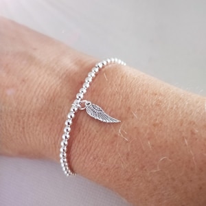 May include: A silver beaded bracelet with a small wing charm. The bracelet is made of small, round beads and is worn on a wrist. The wing charm is detailed and adds a delicate touch to the jewellery.