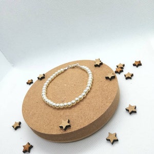May include: A simple pearl bracelet with a silver clasp, displayed on a brown circular surface surrounded by small wooden stars.