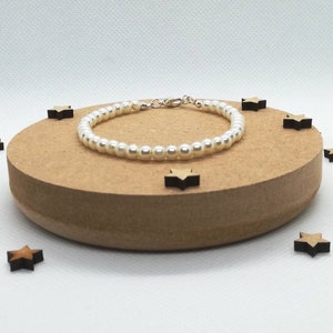 May include: A white pearl bracelet with a silver clasp. The bracelet is on a wooden surface with small wooden stars scattered around it.