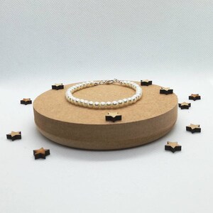 May include: A white pearl bracelet with a silver clasp, displayed on a wooden platform with small wooden stars scattered around it.