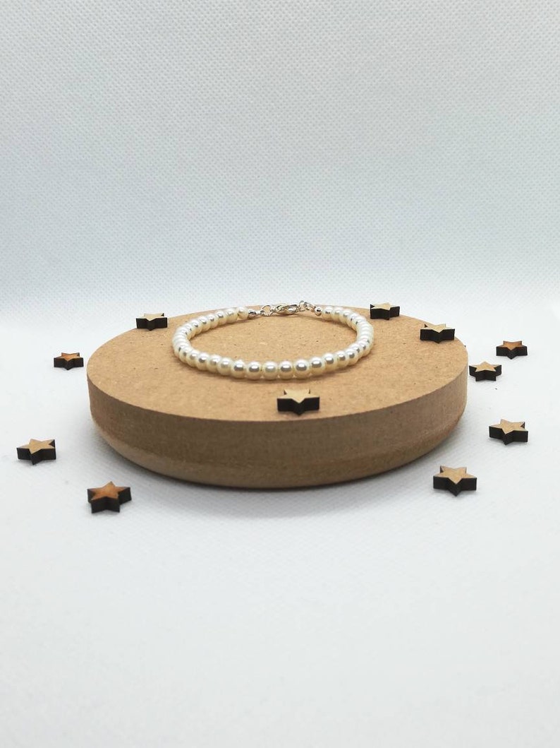May include: A white pearl bracelet with a silver clasp, displayed on a wooden platform with small wooden stars scattered around it.